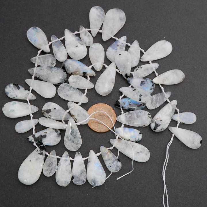 Teardrop-shaped beads on a string with a penny for scale on a dark background