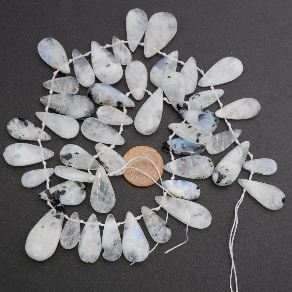 Teardrop-shaped beads on a string with a penny for scale on a dark background