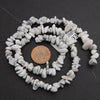 String of white stone beads with a penny for scale on a dark background