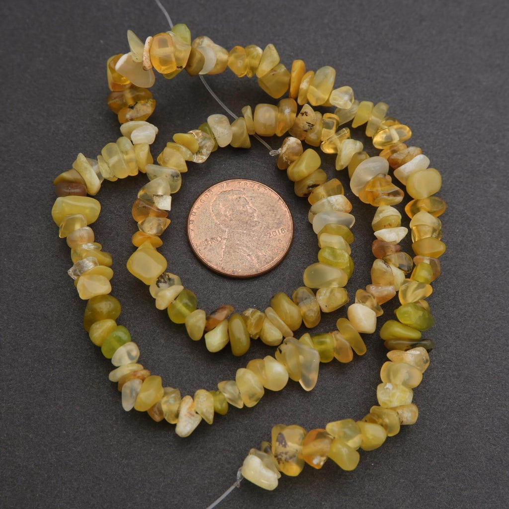 Necklace of yellow and green stone beads with a penny for scale on a dark background