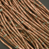 Close-up of rustic copper tube beads on a dark background.