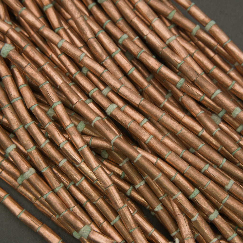 Close-up of rustic copper tube beads on a dark background.