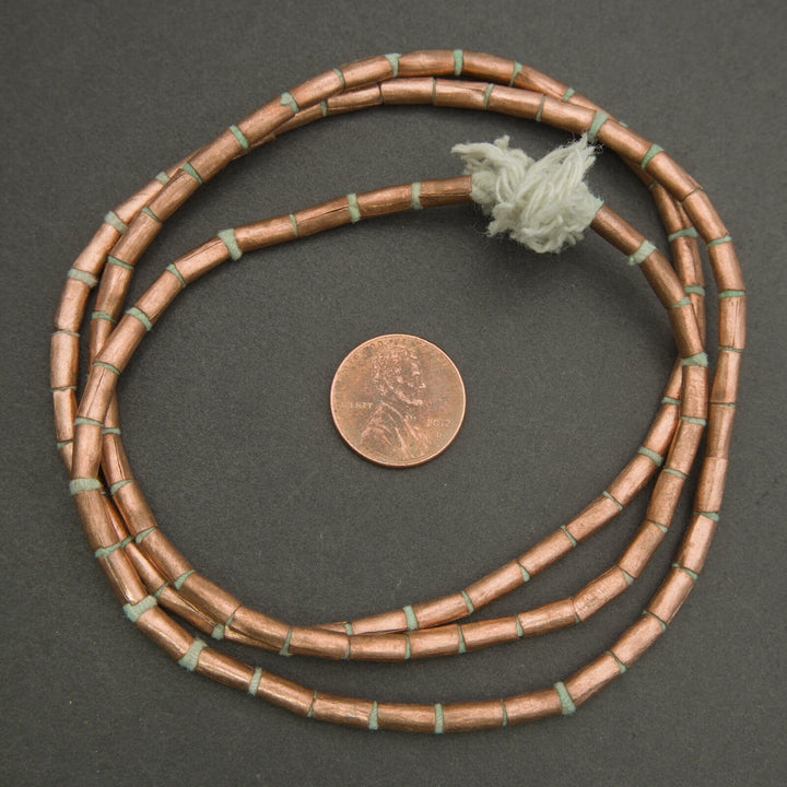 Close-up of rustic copper tube beads on a dark background.