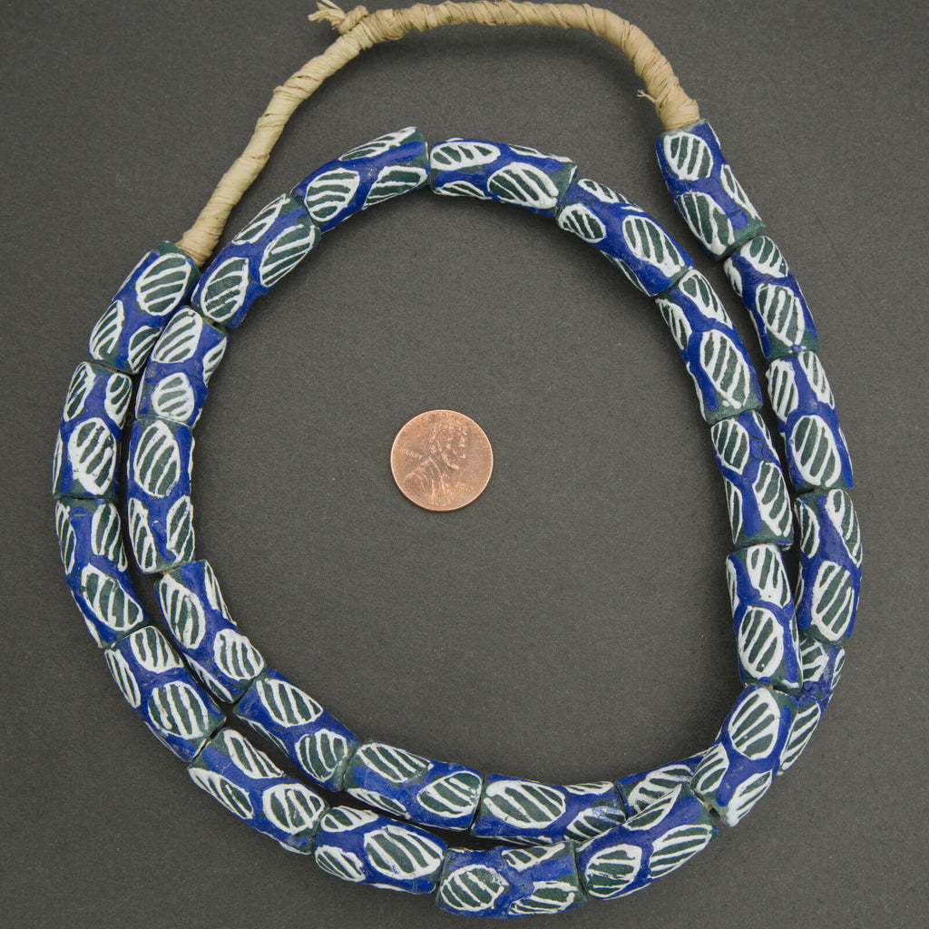 Blue and green patterned beads on a string with a penny for scale on a gray background