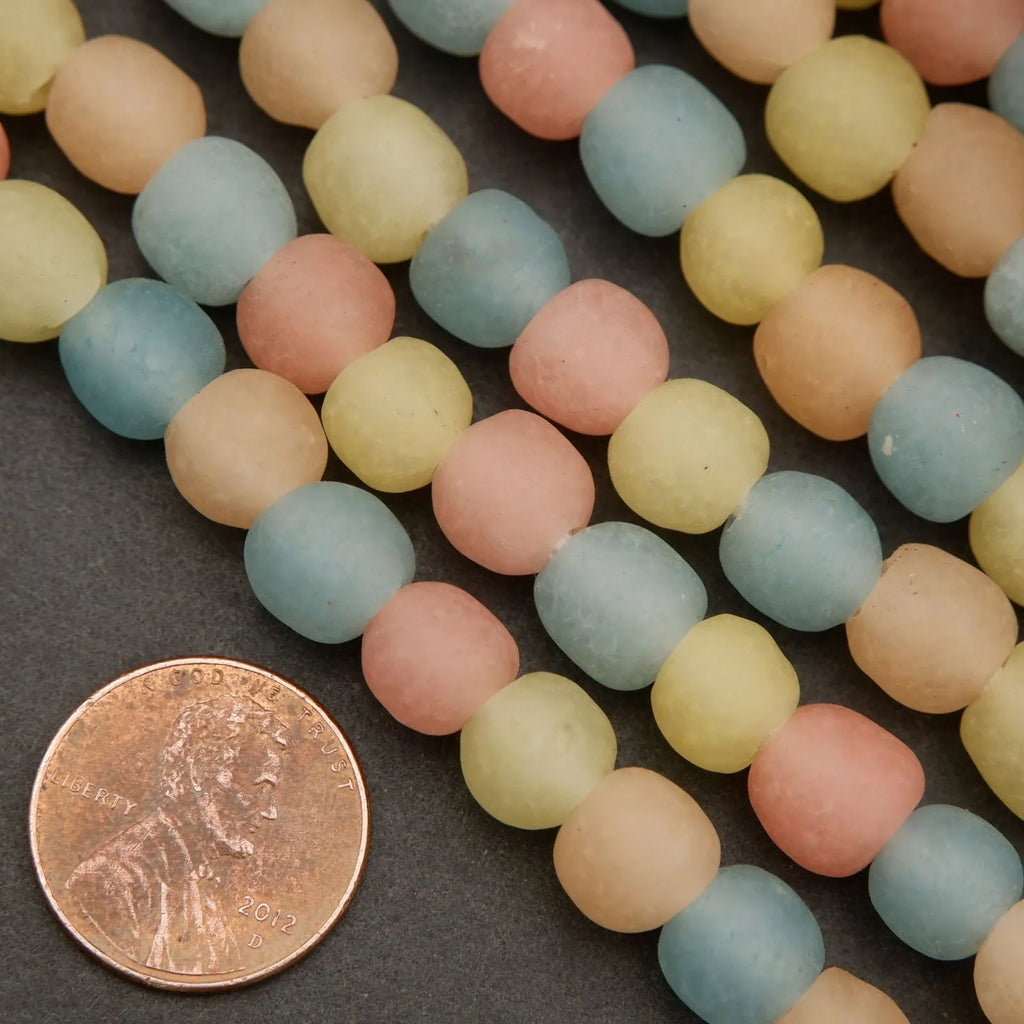 Pastel-colored beads on a dark surface with a penny for scale.
