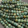 A close-up pile of round turquoise beads with natural green, blue, brown, and black marbling.