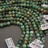 Multiple strands of round turquoise-green stone beads with dark and yellowish marbling, laid out on a gray surface with product tags visible.