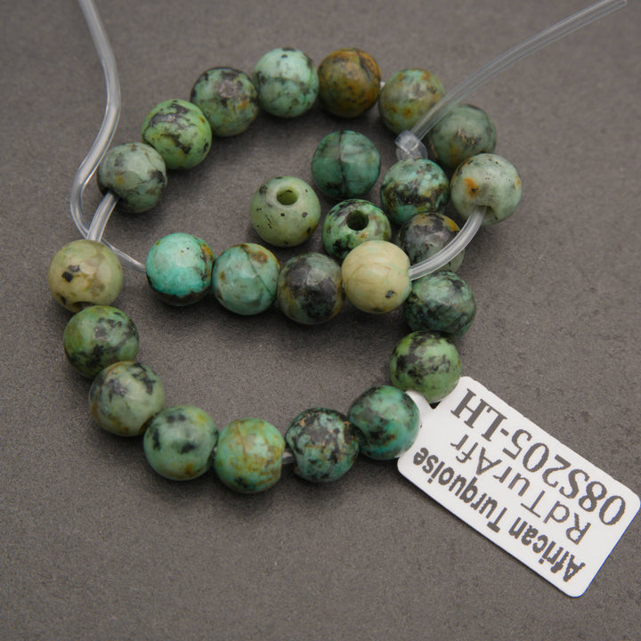 A beaded strand of African turquoise beads with natural green, blue-green, and brown mottled patterns, shown on a gray background with a white product tag.