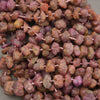 A close-up pile of rough, irregularly shaped beads strung on a cord, showing a mix of earthy brown, terracotta, and dusty rose/pink tones.