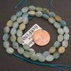 A strand of faceted amazonite oval beads coiled around a penny for scale