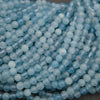 Multiple strands of light blue faceted round beads arranged diagonally on a dark gray surface.