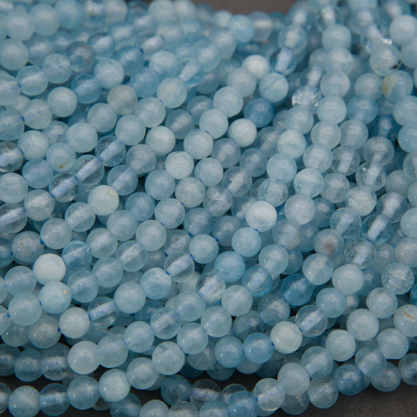 Multiple strands of light blue faceted round beads arranged diagonally on a dark gray surface.
