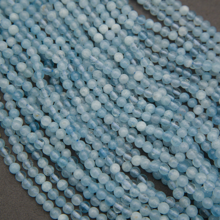 Multiple strands of light blue faceted round beads arranged diagonally on a dark gray surface.