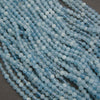 Multiple strands of light blue faceted round beads arranged diagonally on a dark gray surface.