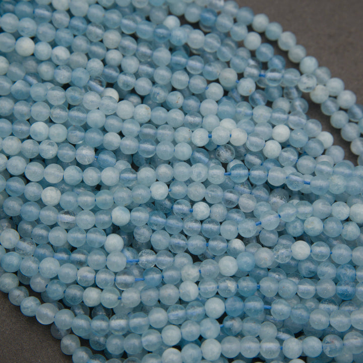 Multiple strands of light blue faceted round beads arranged diagonally on a dark gray surface.