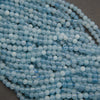Multiple strands of light blue faceted round beads arranged diagonally on a dark gray surface.
