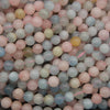 A close-up pile of small round gemstone beads in pastel colors, including pink, blue, pale green, and soft yellow, with some beads showing natural inclusions.