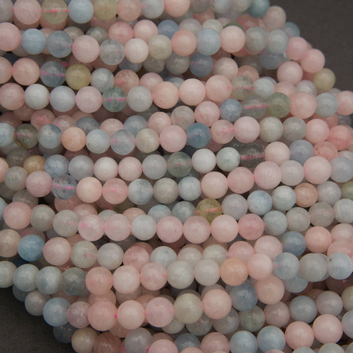 A close-up pile of round, matte gemstone beads in pastel colors, including pink, light blue, pale green, and off-white, filling the frame against a dark background.