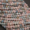 A close-up pile of round, matte gemstone beads in pastel colors, including pink, light blue, pale green, and off-white, filling the frame against a dark background.