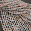 A pile of small round beads in pastel colors, including pink, light blue, pale green, and off-white, with a few translucent yellow beads visible.