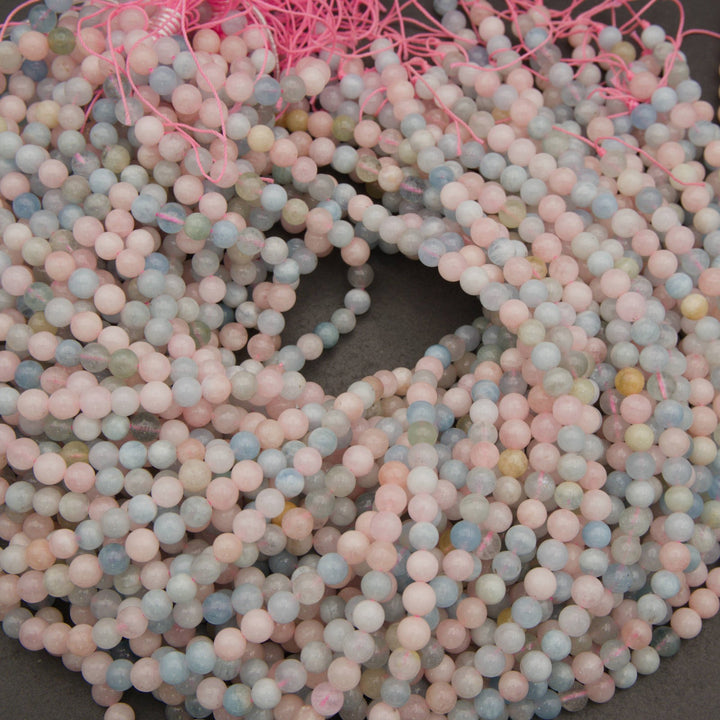 A pile of round gemstone beads in pastel pink, light blue, and soft gray, strung together with bright pink cord on a dark gray surface.