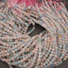 A pile of round gemstone beads in pastel pink, light blue, and soft gray, strung together with bright pink cord on a dark gray surface.