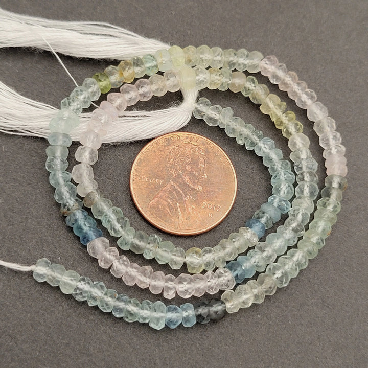 String of small, multicolored beads with a penny for scale on a gray background
