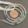 String of small, multicolored beads with a penny for scale on a gray background