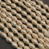 Metallic gold faceted seed beads arranged in diagonal rows on a dark textured background.