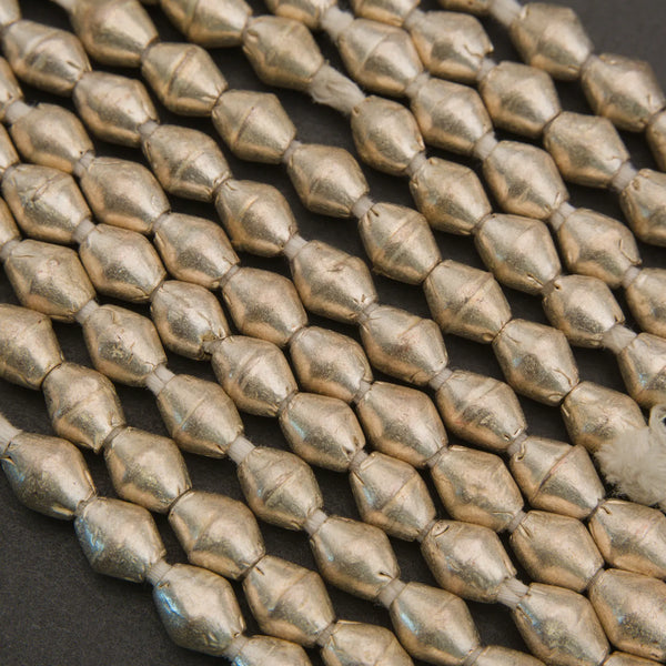 Metallic gold faceted seed beads arranged in diagonal rows on a dark textured background.