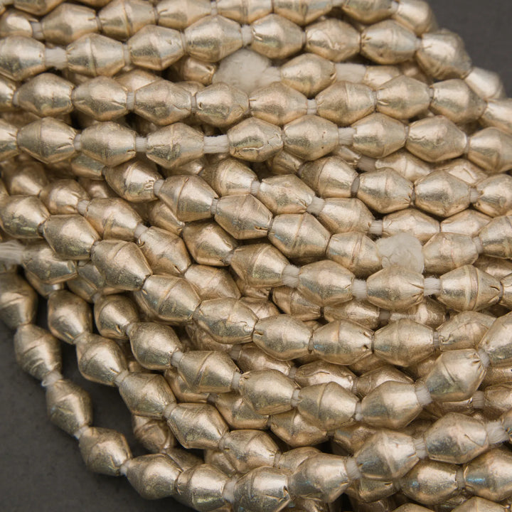 A close-up of metallic gold faceted beads strung on a cord, arranged in a coil against a dark gray background.