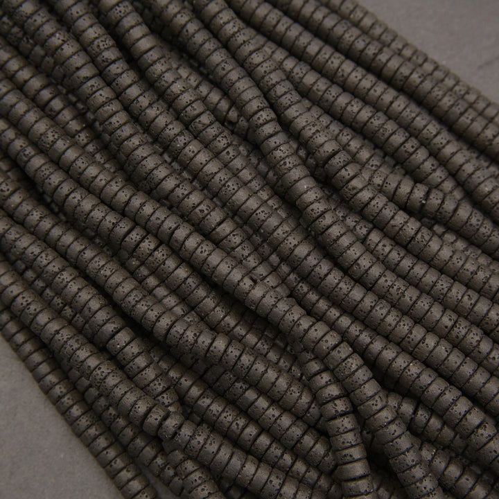 Close-up of black lava rock heishi disk beads featuring flat cylindrical shapes and distinctive volcanic pitting.