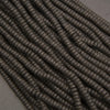 Close-up of black lava rock heishi disk beads featuring flat cylindrical shapes and distinctive volcanic pitting.