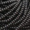 Close-up of glossy black seed beads strung in multiple strands, filling the frame with a reflective, polished surface.