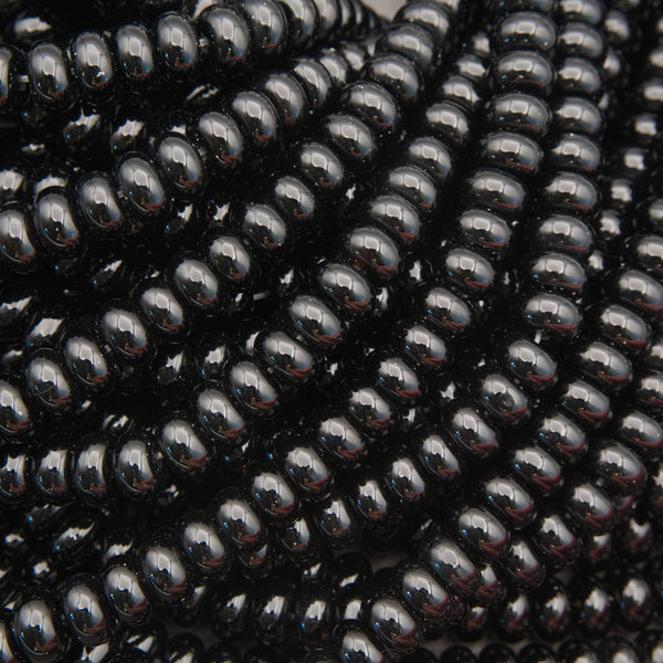 Close-up of glossy black seed beads strung in multiple strands, filling the frame with a reflective, polished surface.