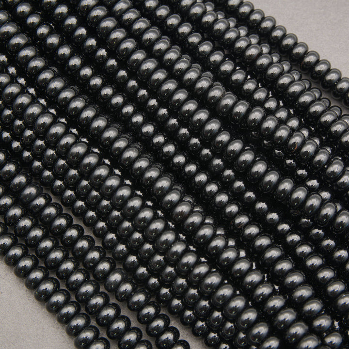 Multiple strands of glossy black round beads arranged diagonally on a light gray background.