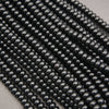 Multiple strands of glossy black round beads arranged diagonally on a light gray background.