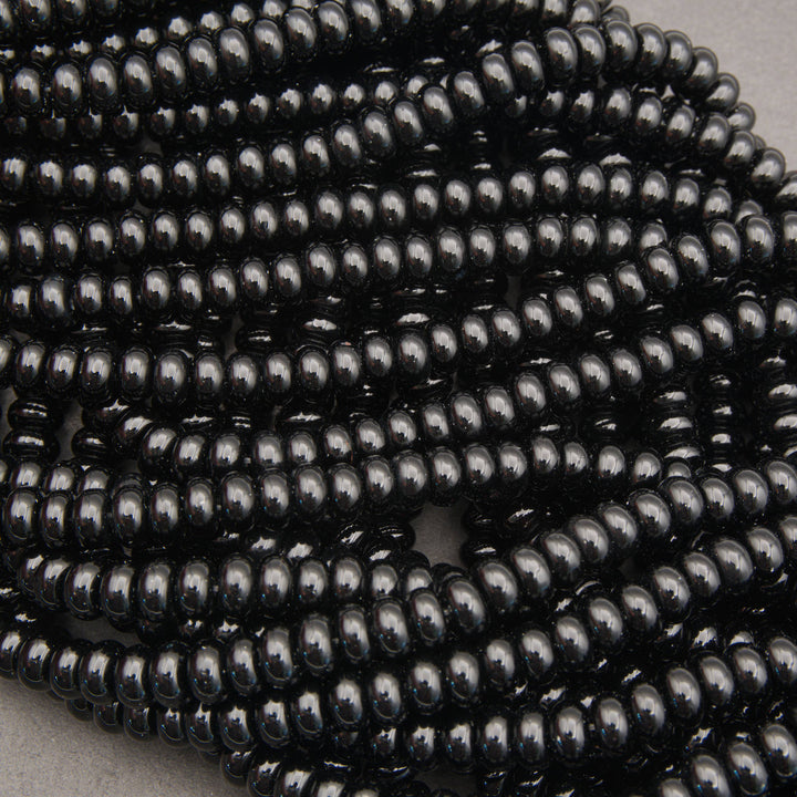 Multiple strands of glossy black seed beads arranged in overlapping rows on a neutral gray surface.
