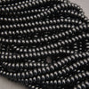 Multiple strands of glossy black seed beads arranged in overlapping rows on a neutral gray surface.