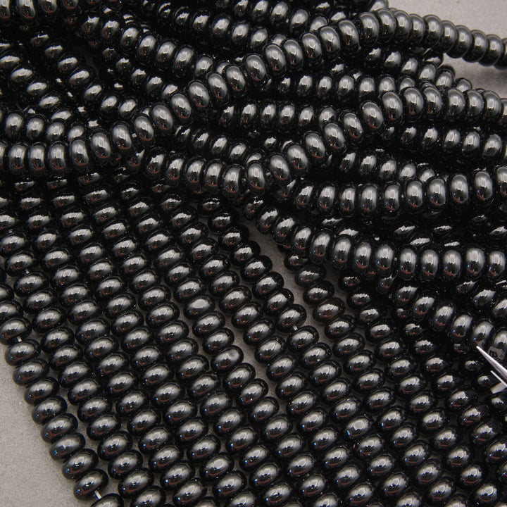 Multiple strands of glossy black oval beads arranged diagonally on a neutral gray background.