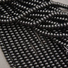 Multiple strands of glossy black oval beads arranged diagonally on a neutral gray background.