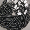 A bulk coil of glossy black seed beads with white product tags attached, photographed on a neutral gray background.