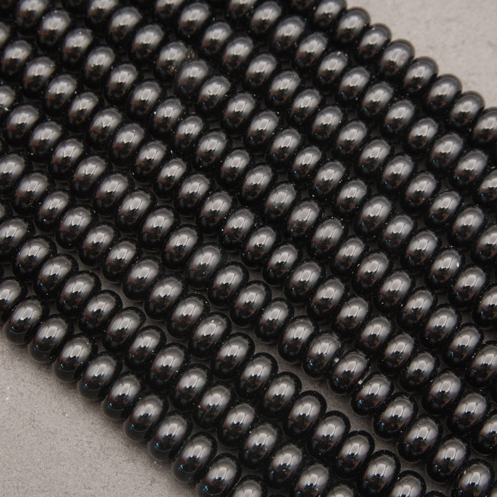 Multiple strands of glossy black oval beads arranged diagonally on a light gray textured surface.