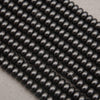 Multiple strands of glossy black oval beads arranged diagonally on a light gray textured surface.