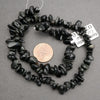 Black stone bead necklace with a penny for scale on a gray background