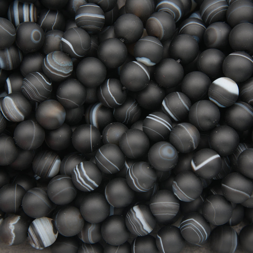 A pile of matte black round beads with natural agate or jasper banding patterns in white, gray, and black.