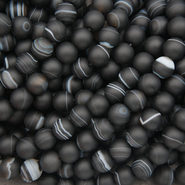 A pile of matte black round beads with natural agate or jasper banding patterns in white, gray, and black.