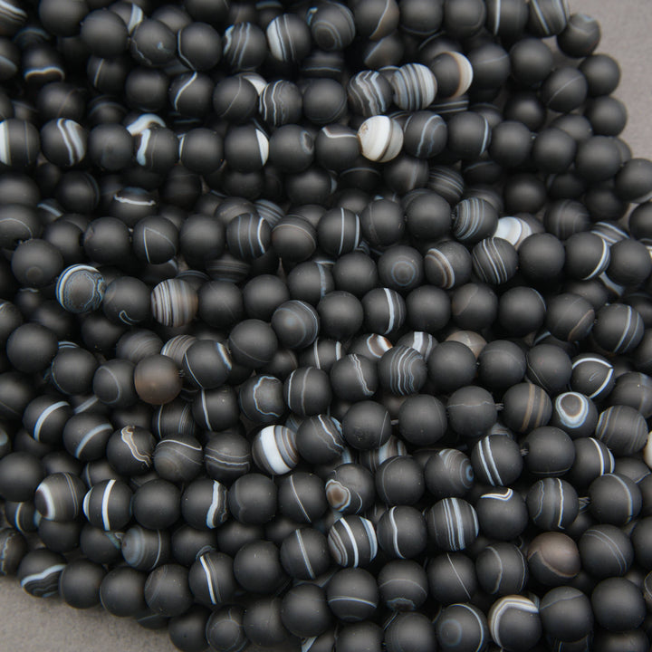 A pile of matte black round beads with white and gray banded agate-like stripes, filling the frame.