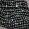 A pile of matte black round beads with white and gray banded agate-like stripes, filling the frame.