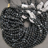 Multiple strands of matte black beaded jewelry, likely necklaces or bracelets, arranged in overlapping coils on a gray surface. Several white product tags with barcode labels are attached near the top.